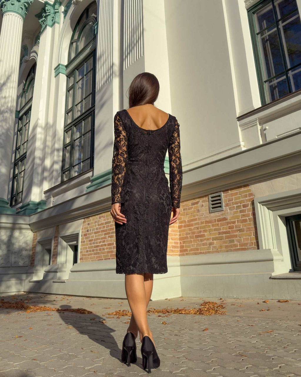 Rochie neagra din dantelă cu mâneci lungi, vedere din spate, exterior clădire.