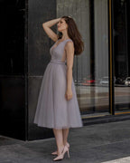 Rochie de ocazie gri midi cu decolteu și șiret la spate, din satin regal și tull, purtată de o femeie.