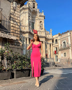 Rochie eleganta roz cu decolteu și două slituri, purtată pe stradă în fața unei clădiri impunătoare.